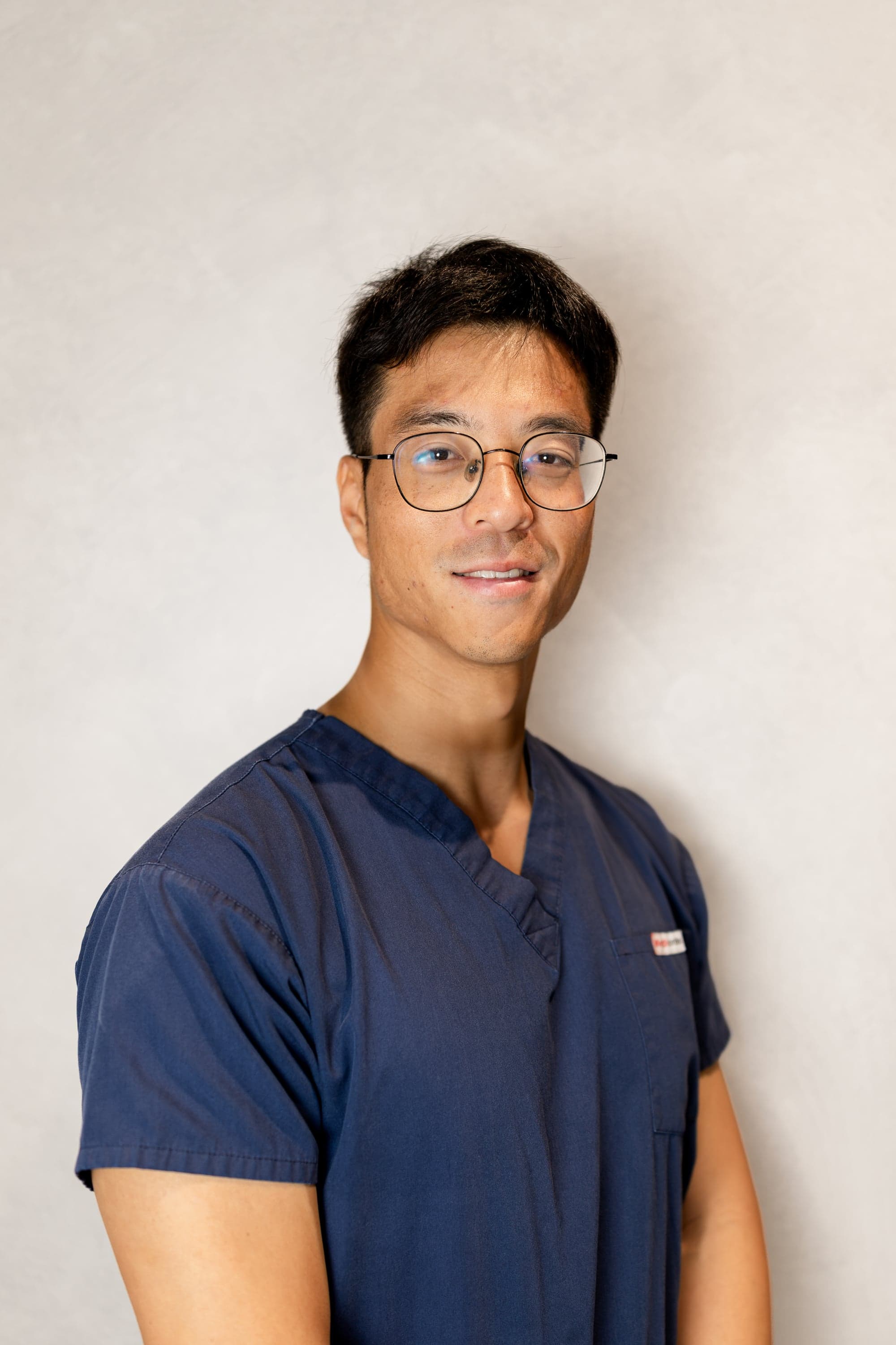 Dr John Huang, Associate Dentist at Joyner Family Dental, smiling in navy scrubs